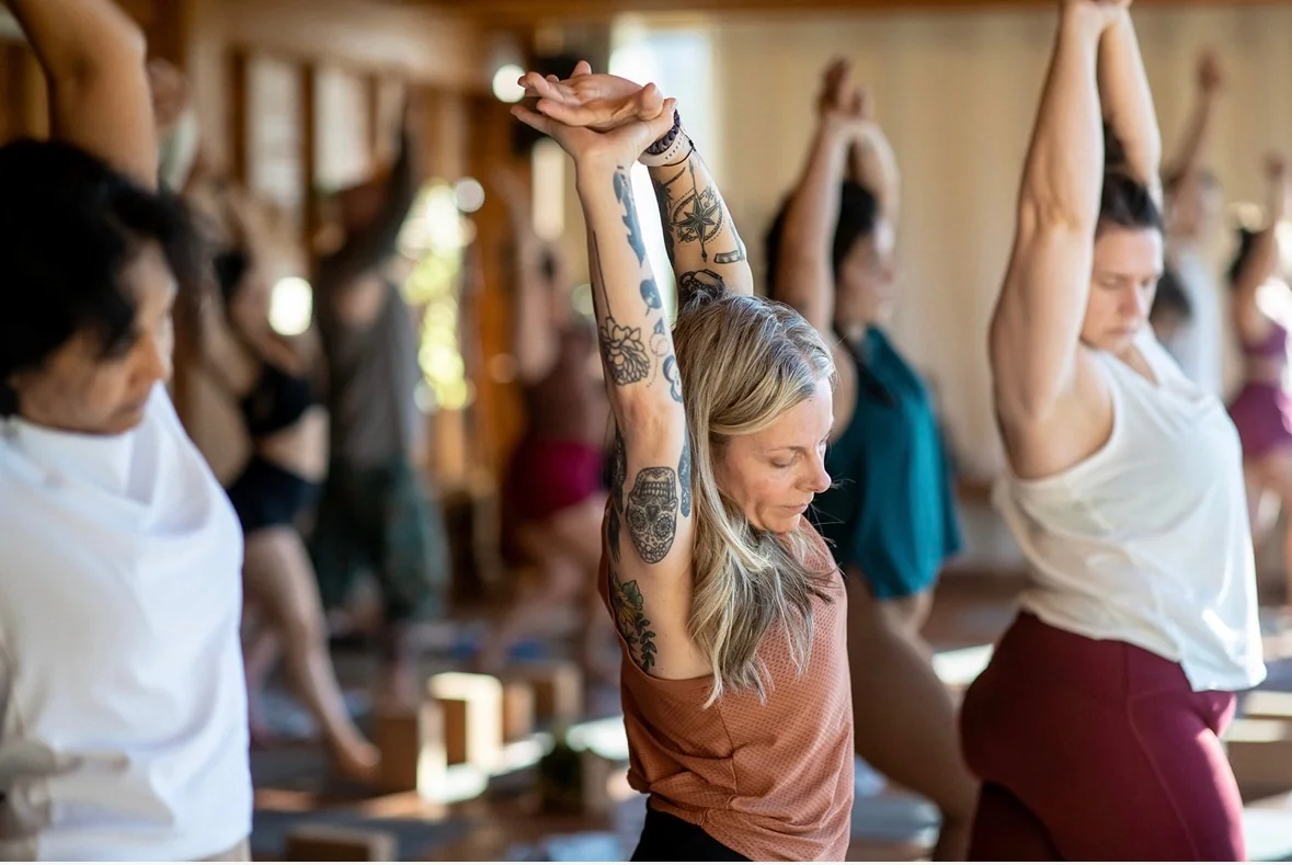 Jennifer Dessert reaching overhead alongside other yoga practitioners.