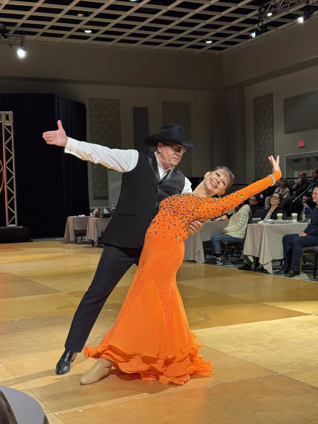 Shari dancing with a partner in an orange ballroom dress.